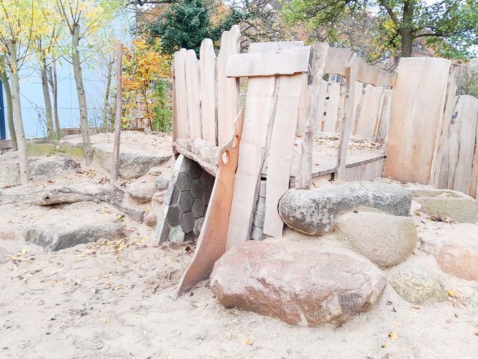 ein Holzspielplatz mit Bäumen und Felsen im Hintergrund - Spielplatzprüfung Franziska Müller aus Lüchow im Wendland