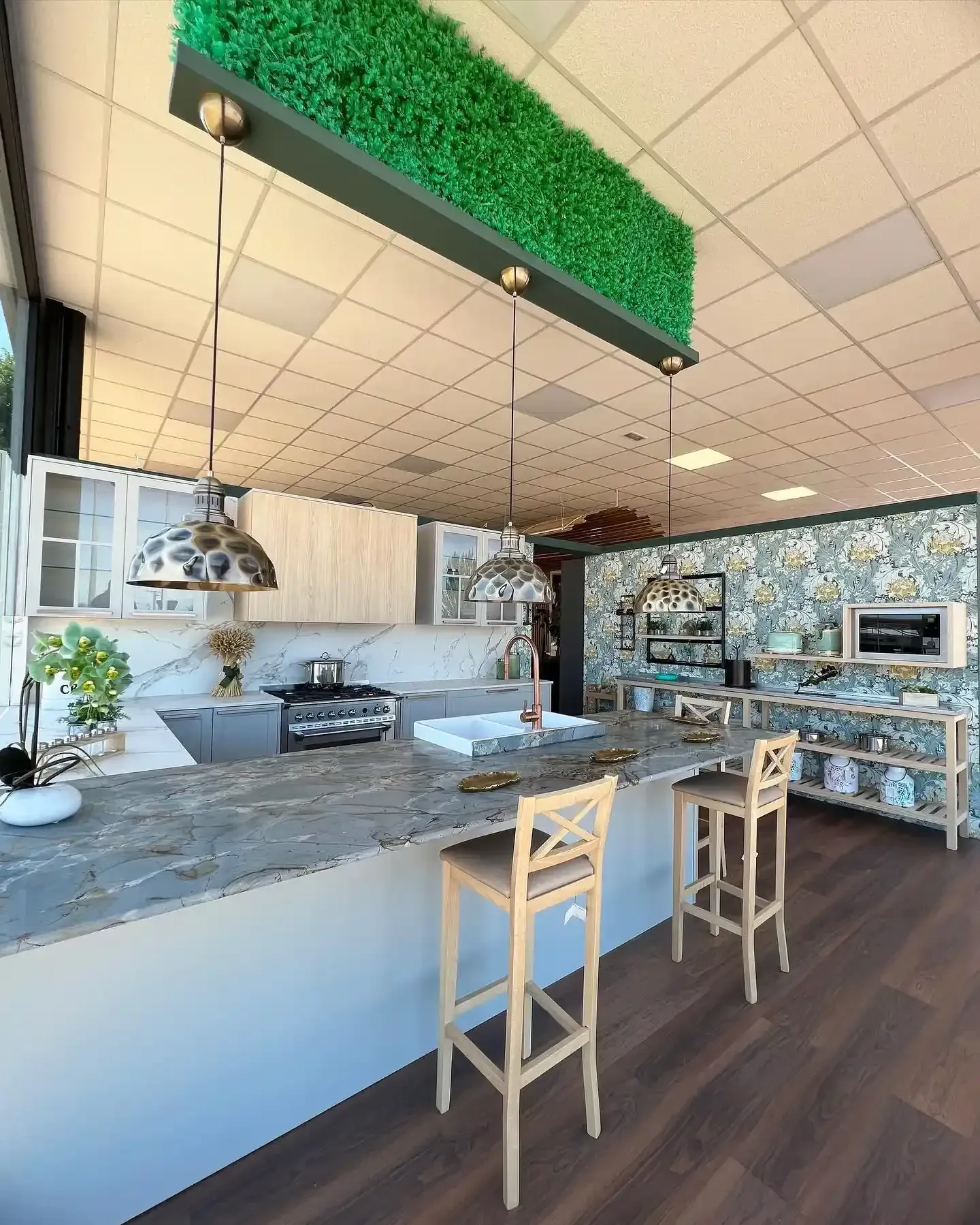 Interior de cafetería moderna con mostrador de mármol, taburetes altos y decoración de pared verde.