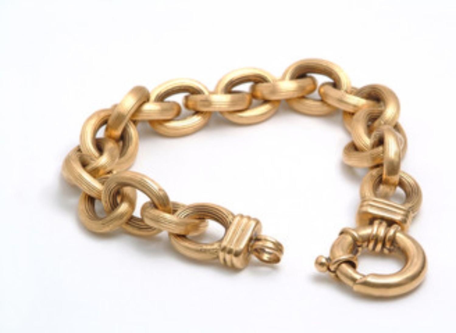 Pulsera de cadena de color dorado con grandes eslabones ovalados y cierre decorativo sobre fondo blanco.