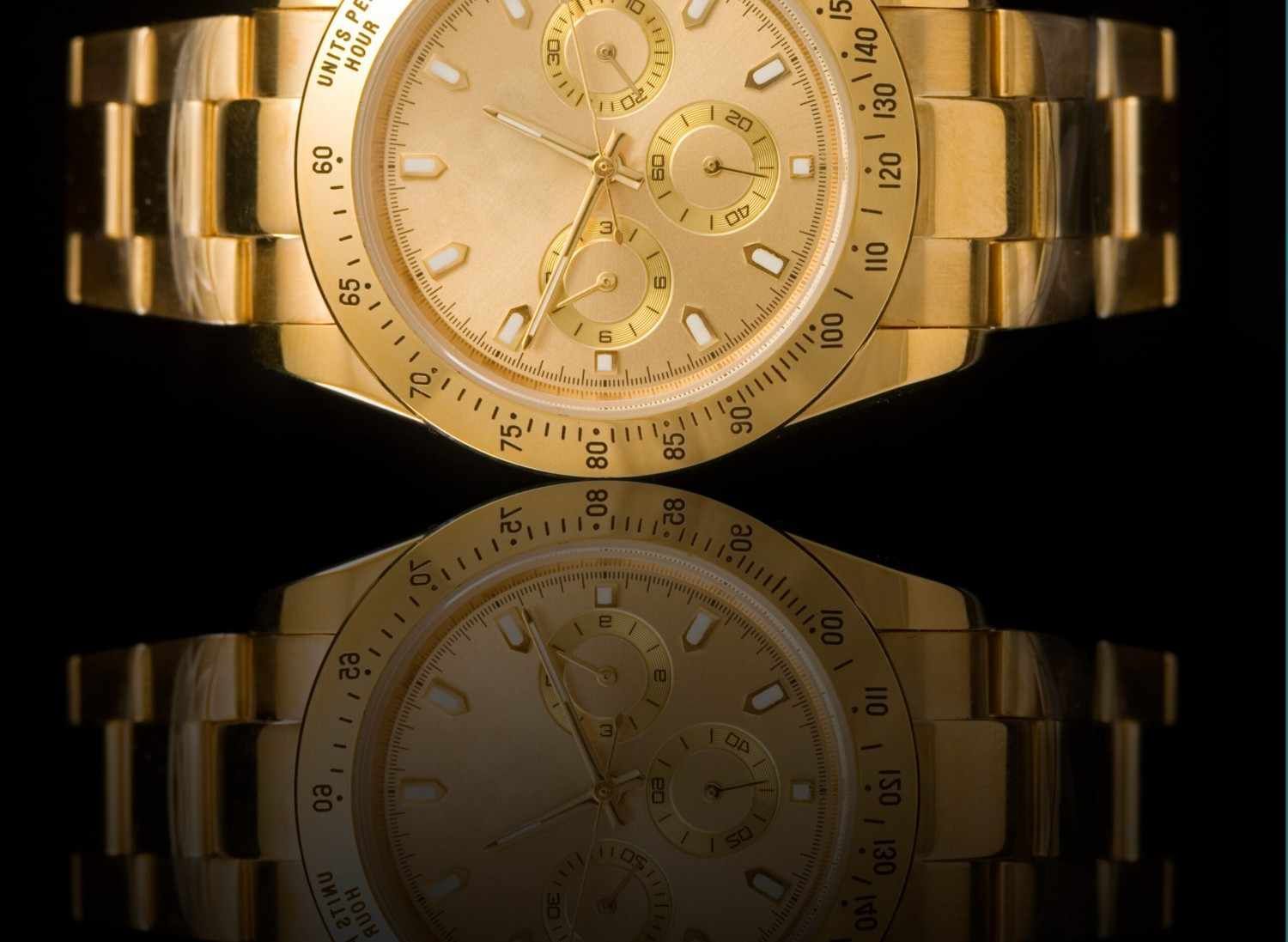 Reloj de pulsera dorado que se refleja en una superficie negra.