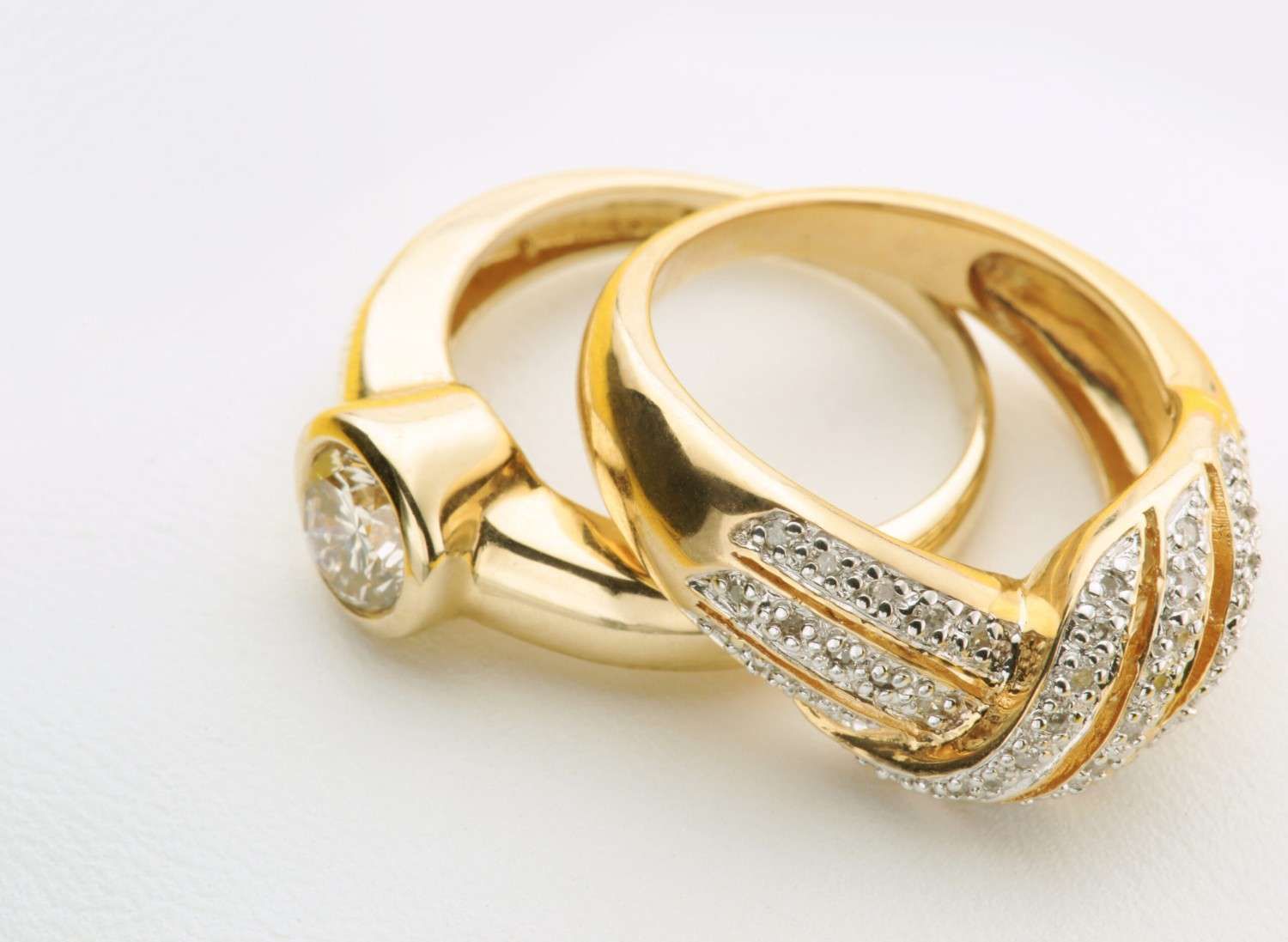 Dos anillos de oro con diamantes incrustados sobre una superficie blanca.