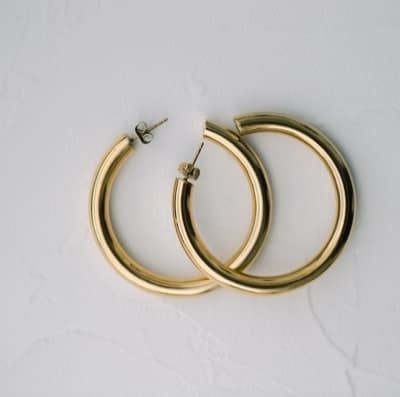 Par de pendientes de aro dorados sobre superficie blanca texturizada.