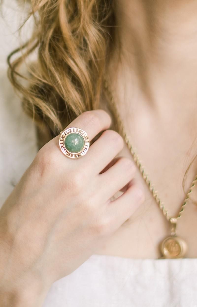 Mano de mujer con un anillo grande con piedra verde y marco dorado. Collar de oro.