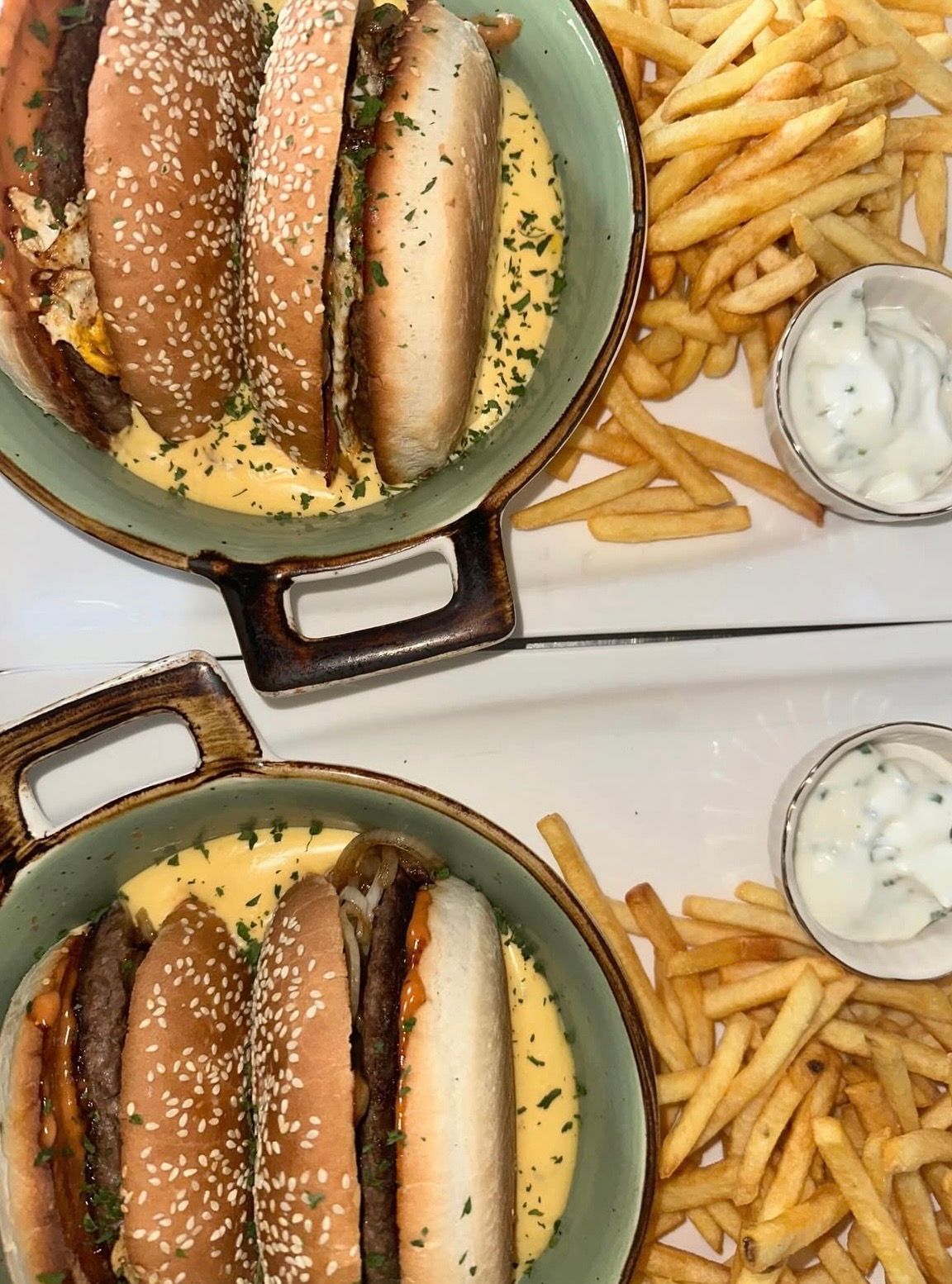 Zwei Teller mit Mini-Burgern, überbacken mit geschmolzenem Käse, serviert mit Pommes frites und einer Beilage weißer Dip-Sauce.