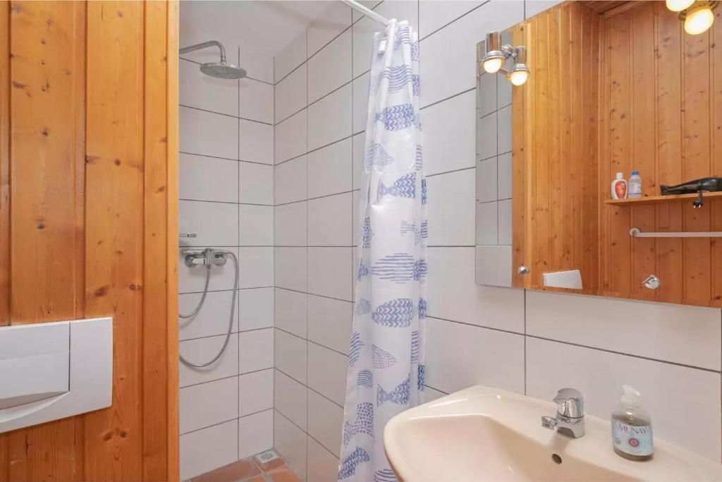 Baño con pared de paneles de madera y ducha, paredes de azulejos blancos, lavabo, cortina de ducha.
