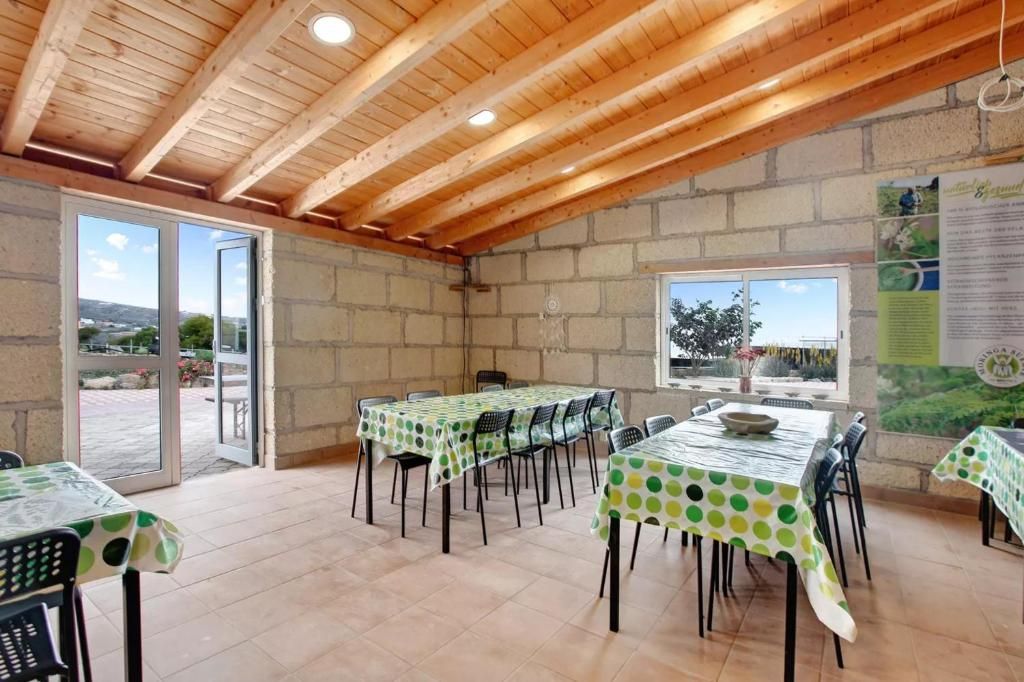 Un comedor al aire libre con mesas, sillas y techo de madera. Tiene paredes de bloques, grandes puertas de cristal y ventanas.