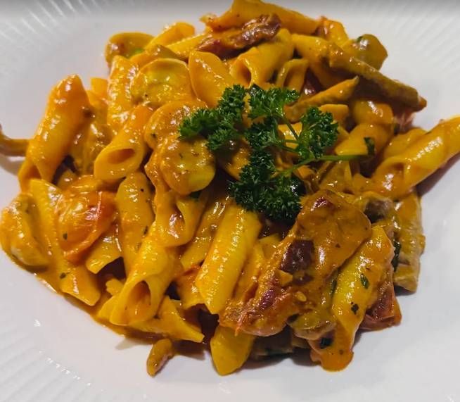 Cremige Penne-Nudeln mit Gemüse und Petersiliengarnitur auf einem weissen Teller