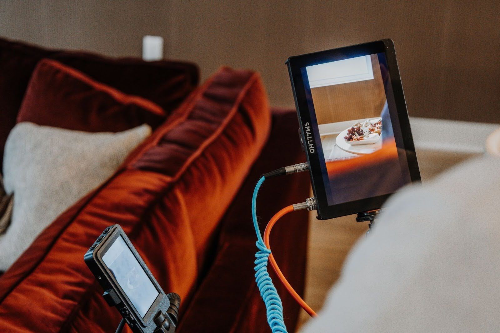A portable production monitor and a handheld recorder on a stand next to a velvet sofa during a video shoot.