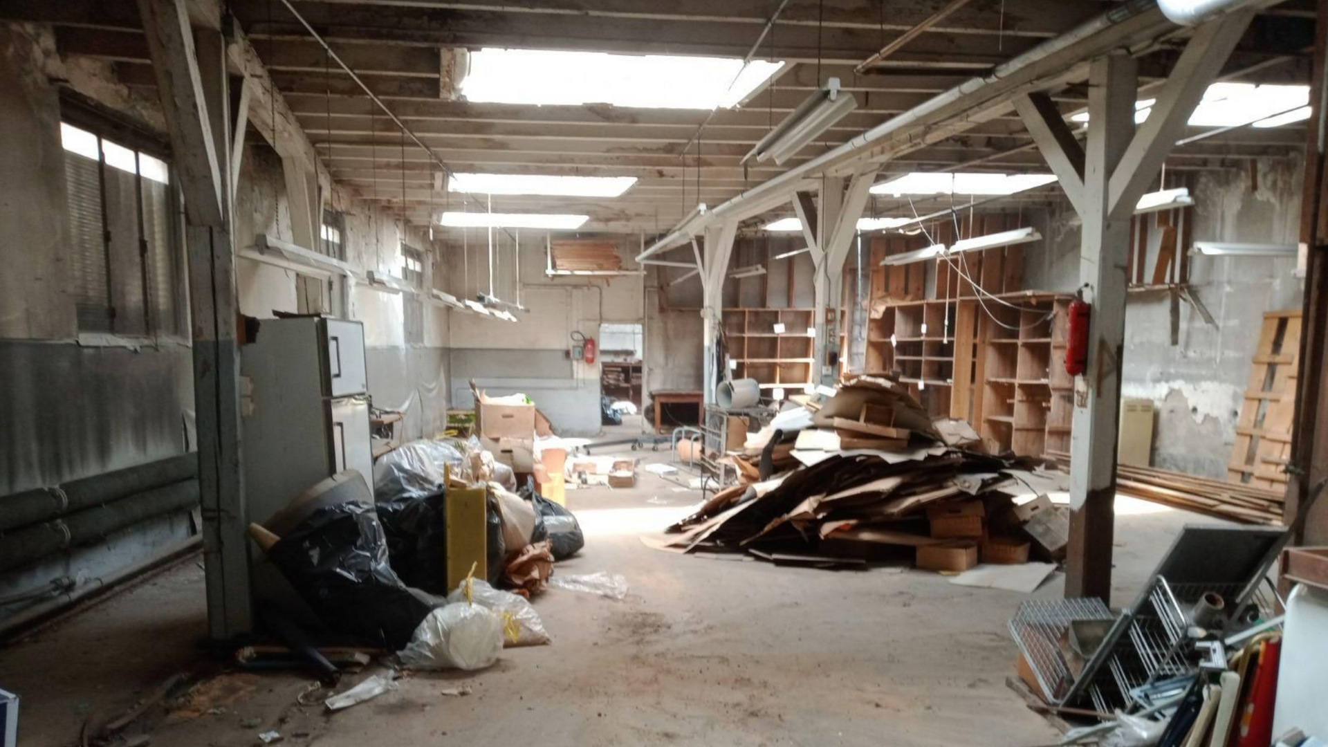 Intérieur d'un atelier délabré, montrant des poutres apparentes, des débris et des murs démolis.