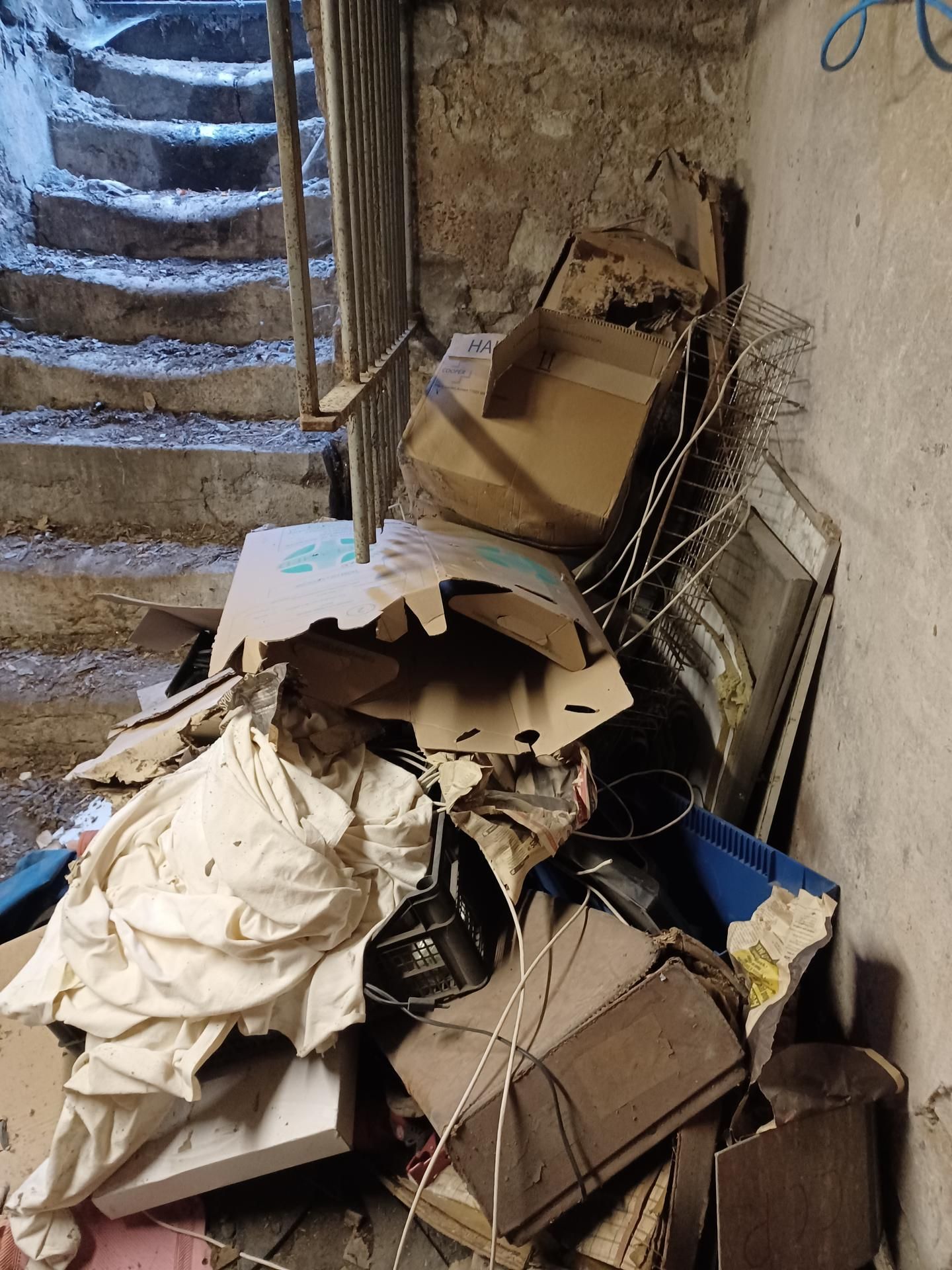 Un tas d'objets jetés près d'un escalier en béton, dans un espace faiblement éclairé. Ceci est avant l'intervention du professionnel.