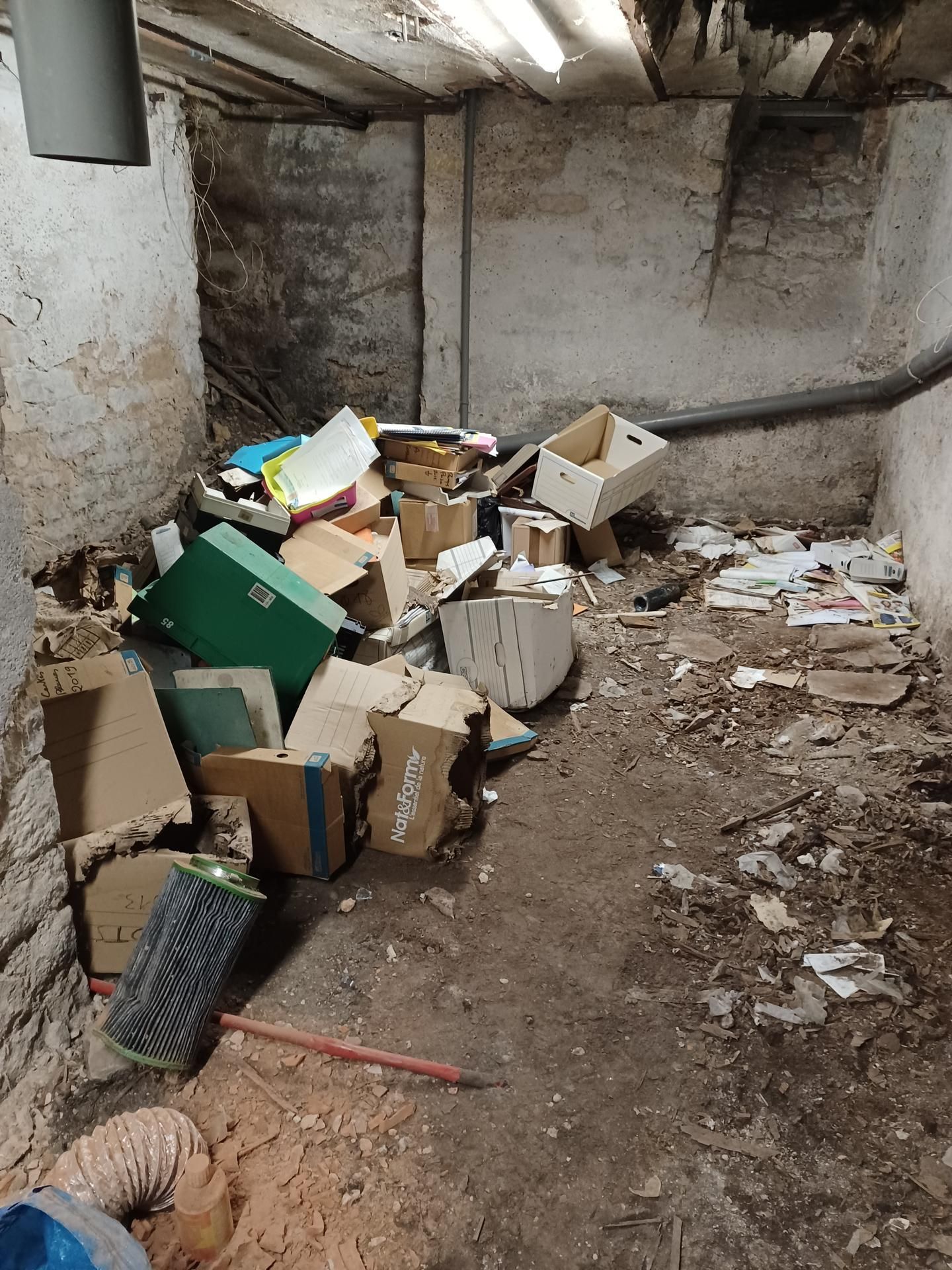 Sous-sol encombré de cartons, de débris et de tuyaux apparents. Ceci est avant l'intervention du professionnel.