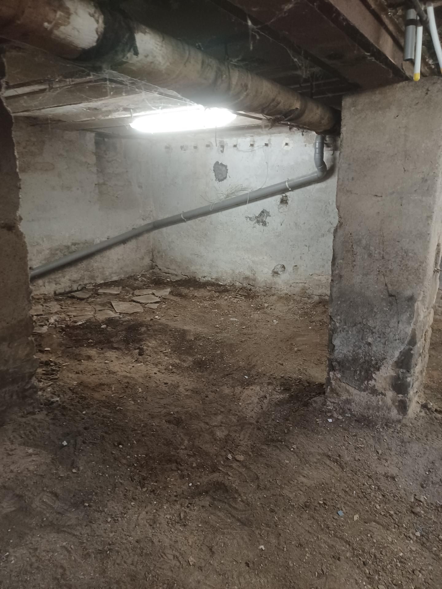 Intérieur d'un sous-sol avec piliers de soutien, tuyaux et sol en terre battue qui a été nettoyé. Sous-sol encombré de cartons, de débris et de tuyaux apparents. Ceci est après l'intervention du professionnel.