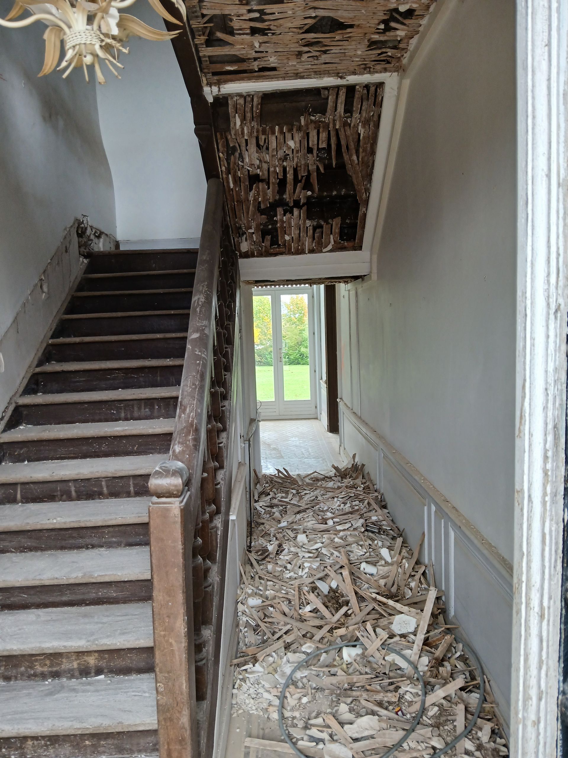 Vue intérieure d'un escalier en rénovation ; débris au sol, plafond endommagé, ceci est avant l'intervention du professionnel.