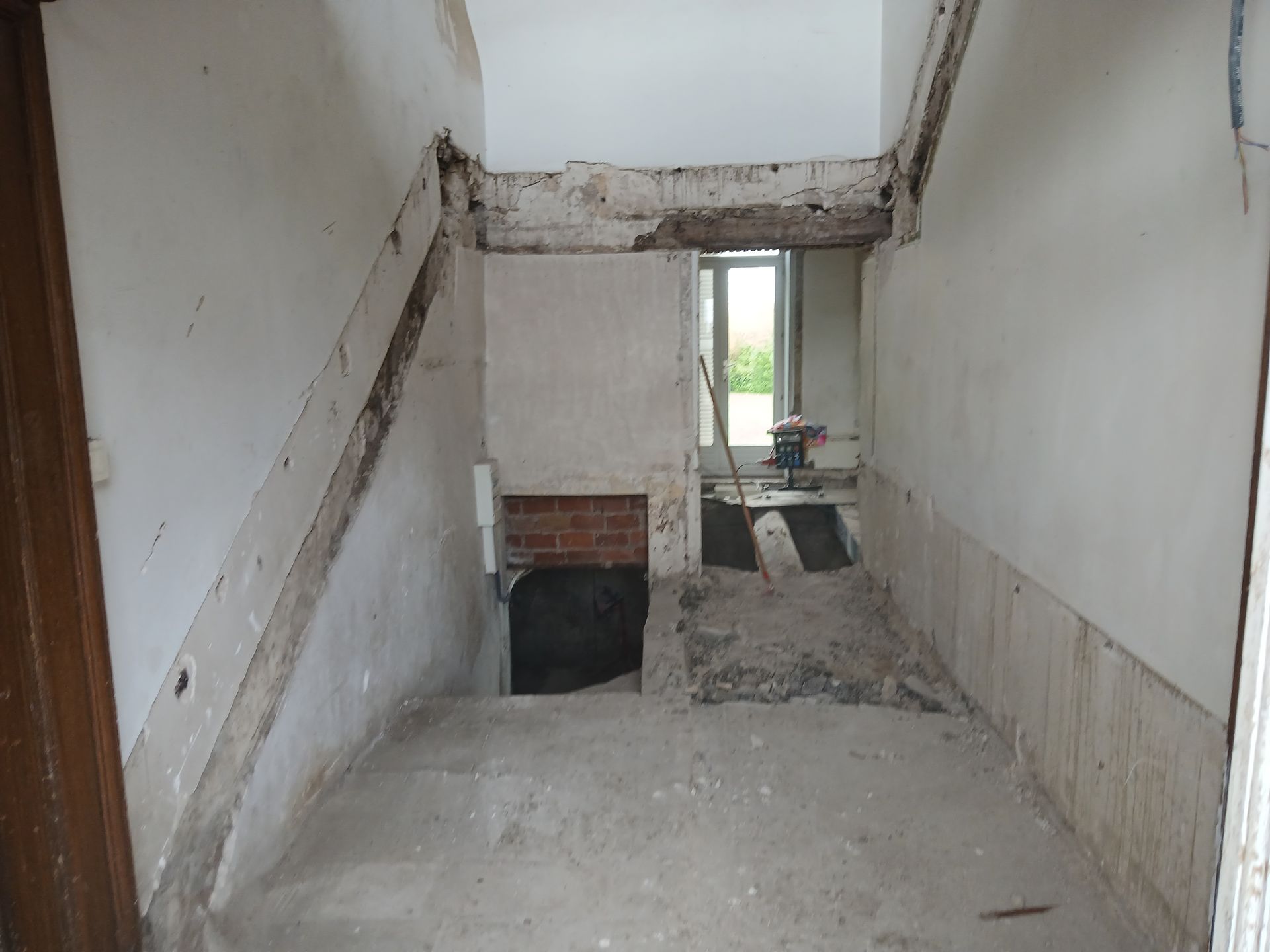 Couloir intérieur en rénovation : poutres apparentes, briques et fenêtre. Murs partiellement démolis. Ceci est après l'intervention du professionnel.