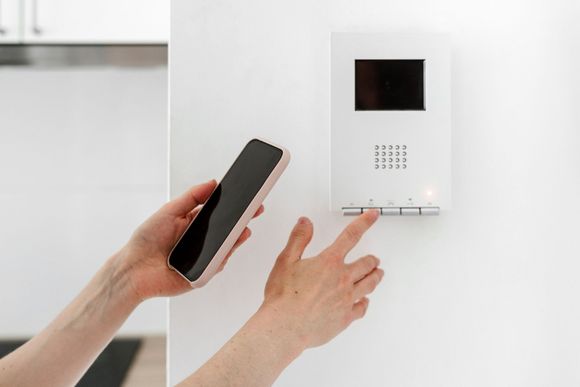 Persona que utiliza un teléfono inteligente y un sistema de intercomunicación montado en una pared blanca.