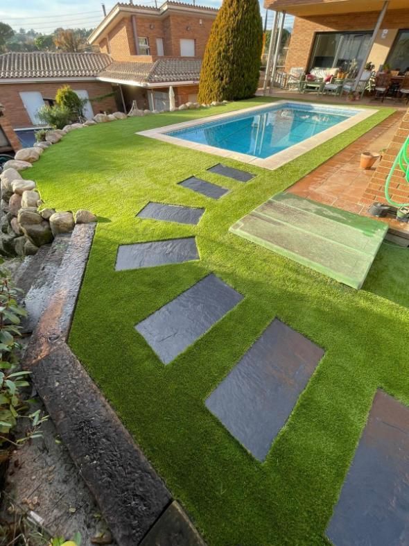 Un patio trasero con césped artificial, una piscina, un camino de adoquines de piedra