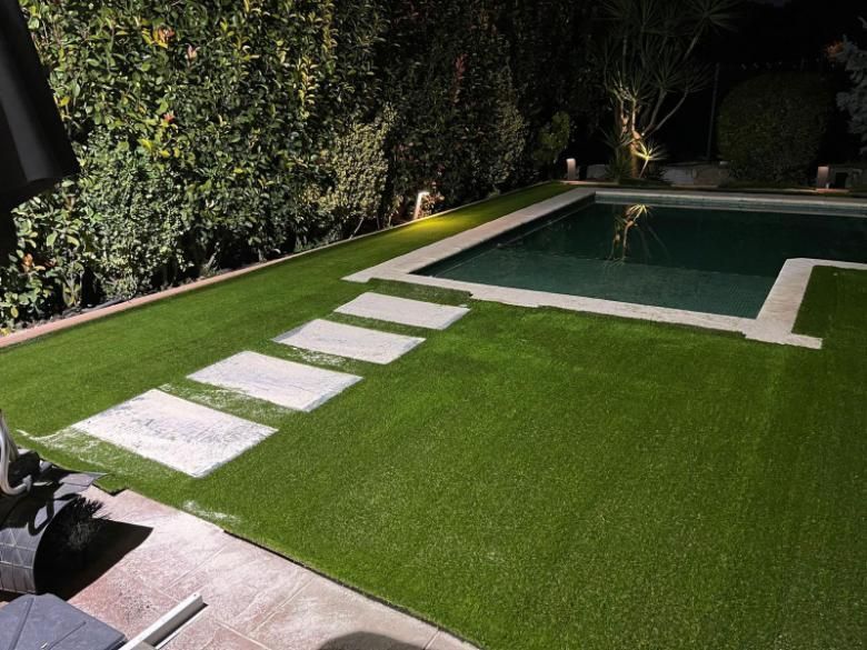 Una piscina en el patio trasero, bordeada de césped artificial verde y un sendero de cuatro adoquines 