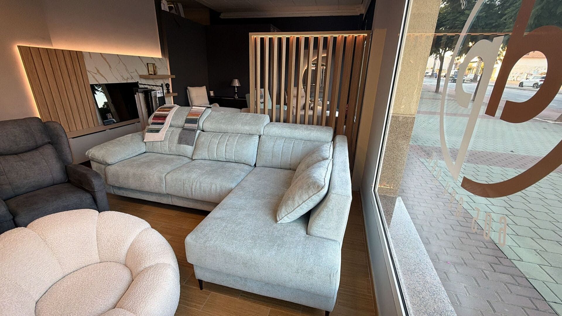 El interior de una tienda de muebles exhibe un sofá seccional azul claro, una silla blanca afelpada y un sillón reclinable.