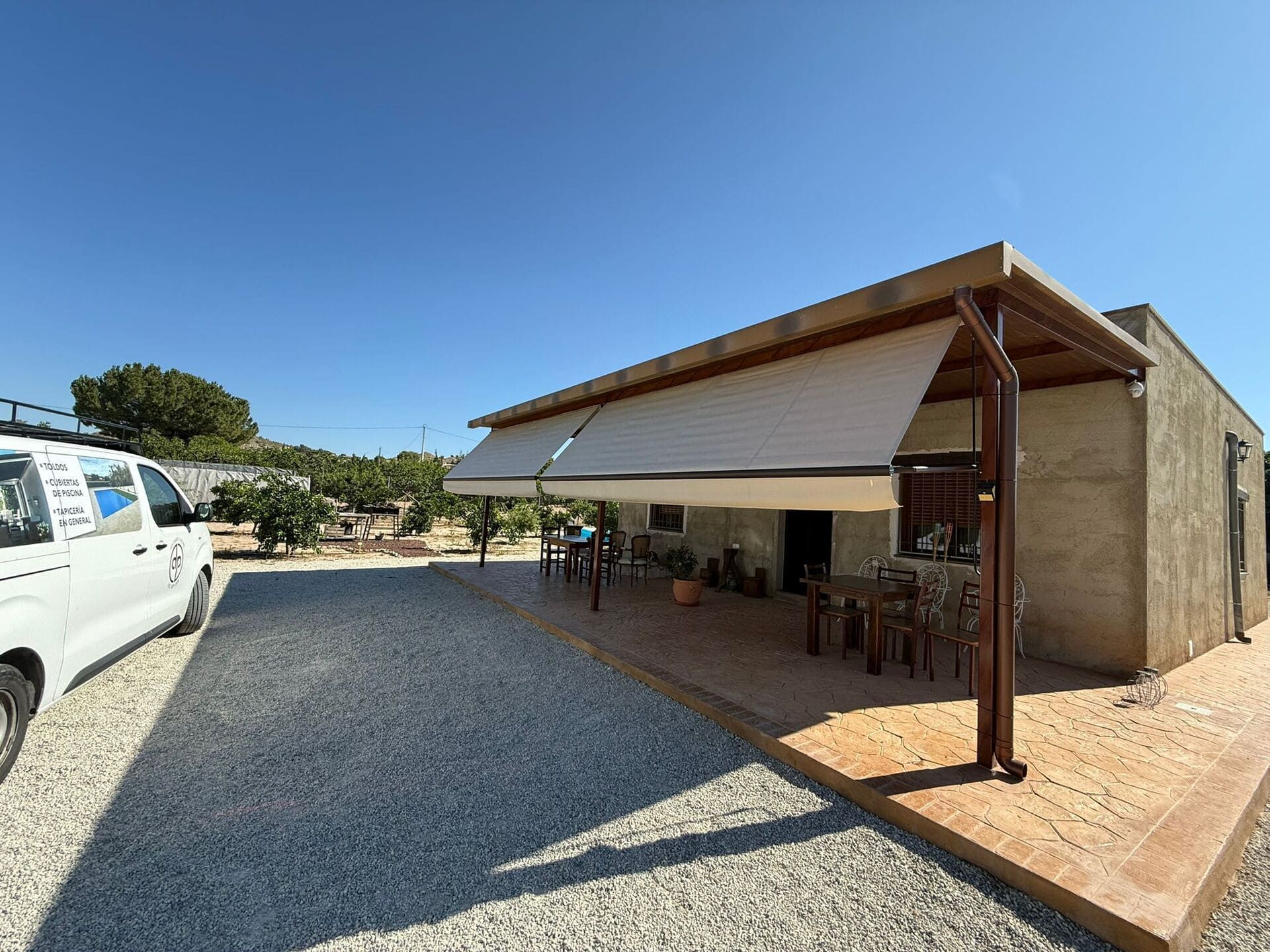 Una zona de patio sombreada con toldo, asientos y entrada de grava.