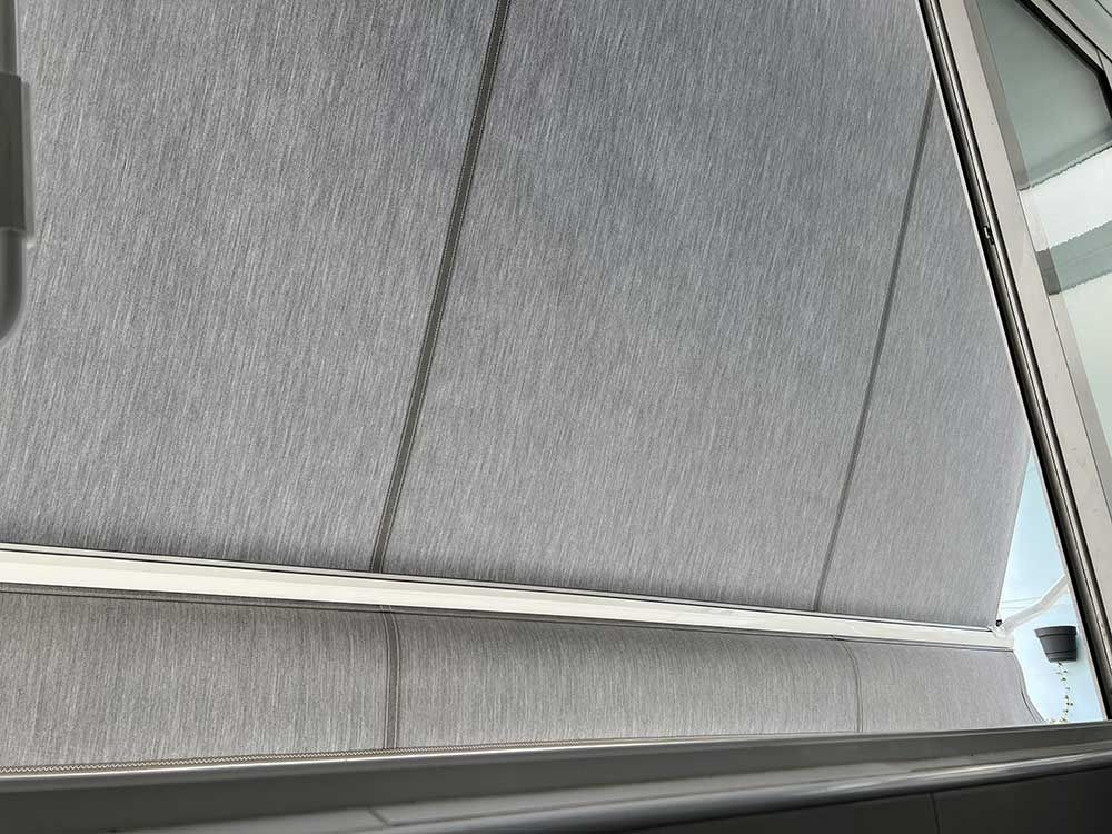 Primer plano de una persiana enrollable gris parcialmente corrida frente a una ventana.