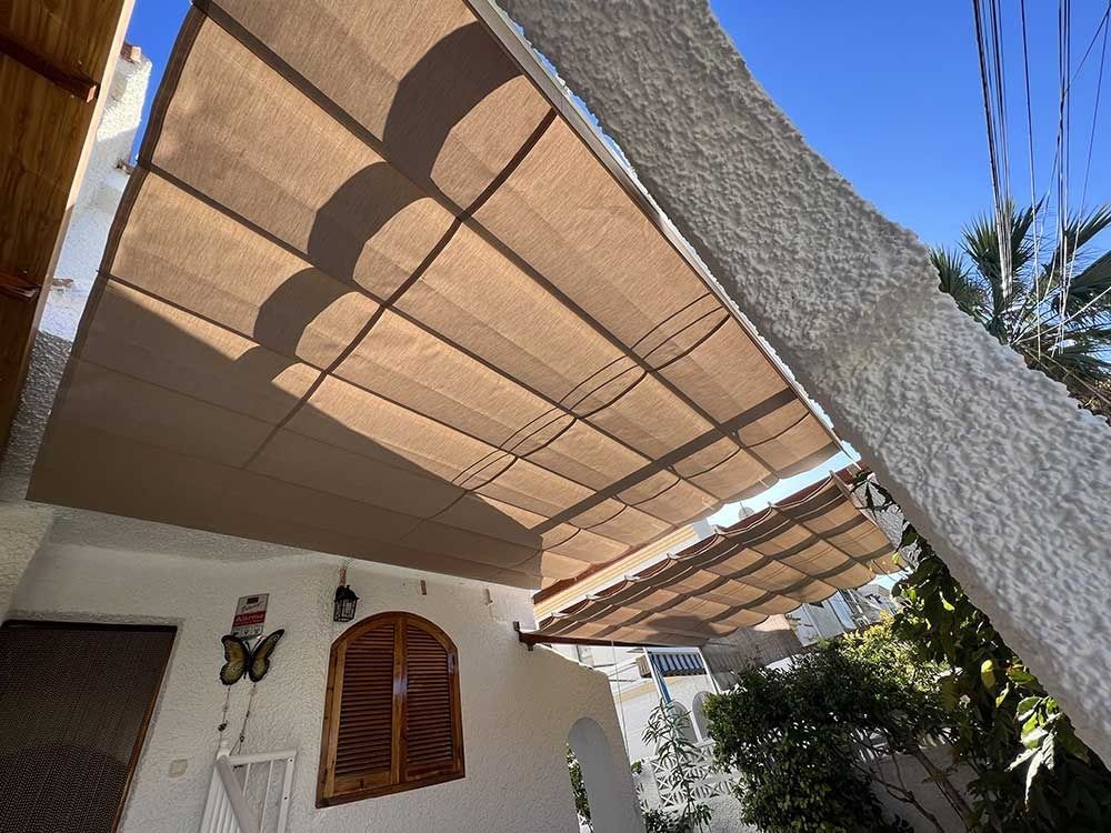 Toldo beige sobre un edificio blanco con ventana marrón y un cielo azul brillante.