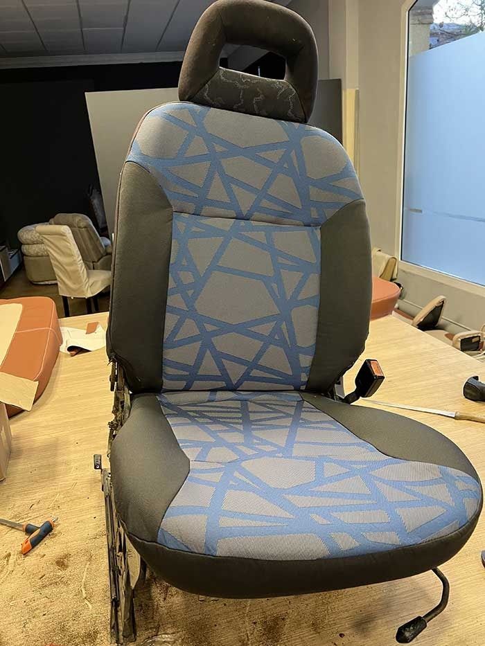 Asiento de coche con estampado geométrico azul y detalles en negro en un entorno de taller.