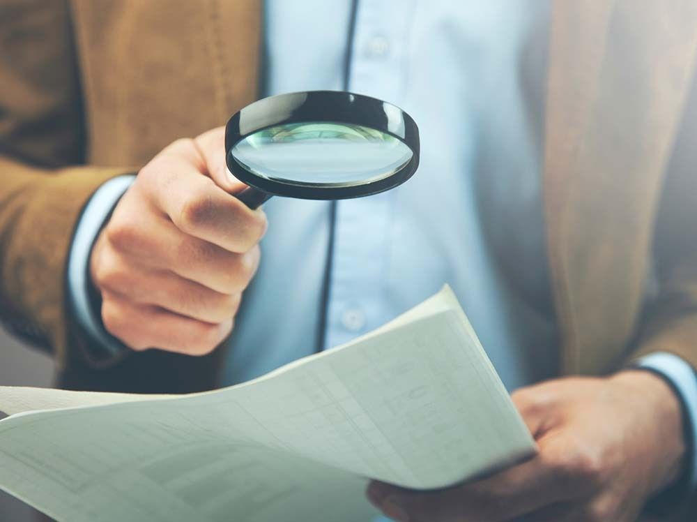 Persona sosteniendo una lupa sobre un documento.