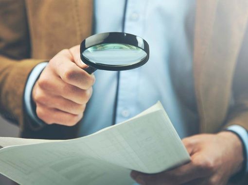 Persona sosteniendo una lupa sobre un documento.