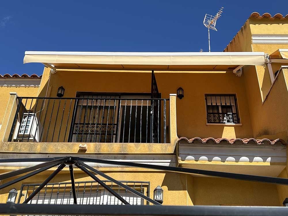 Edificio amarillo con balcón, toldo y barandilla negra contra un cielo azul.