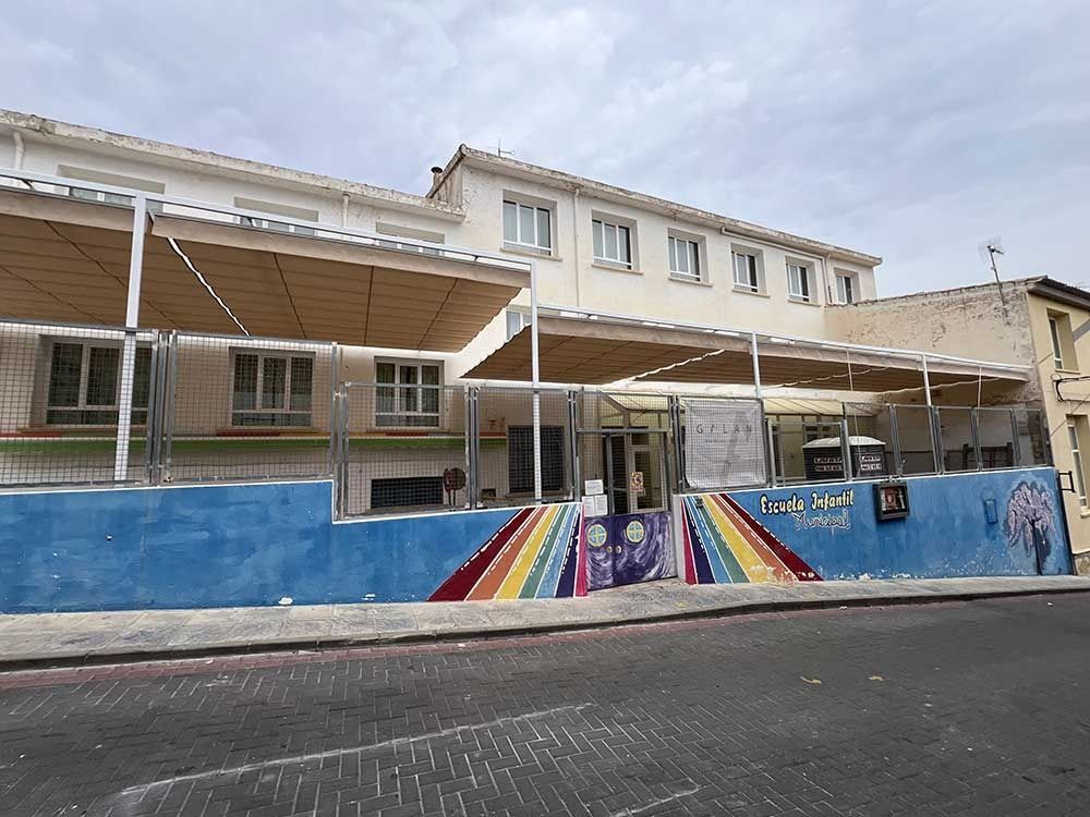 Edificio escolar con toldo y colorido mural en pared azul.