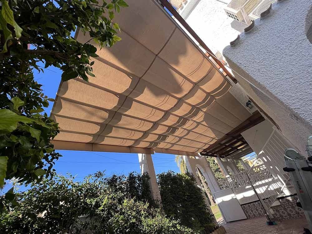 Un toldo color canela da sombra a un patio, con el cielo azul a la vista.