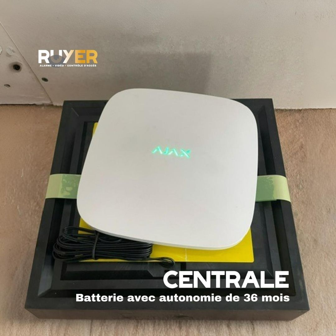 Système de sécurité Ajax blanc sur une base jaune et noir, avec câble intégré. Inscriptions : « Centrale » et « Batterie avec autonomie de 36 mois ».