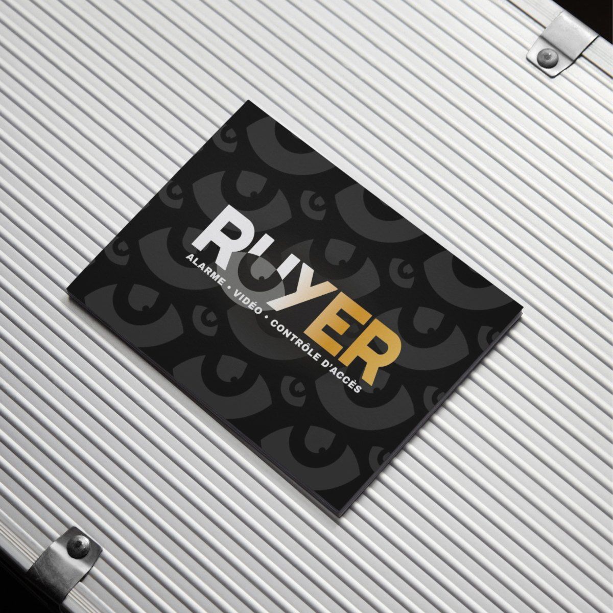 Carte de visite noire sur support métallique argenté avec le logo « Ruyer » en blanc et or.
