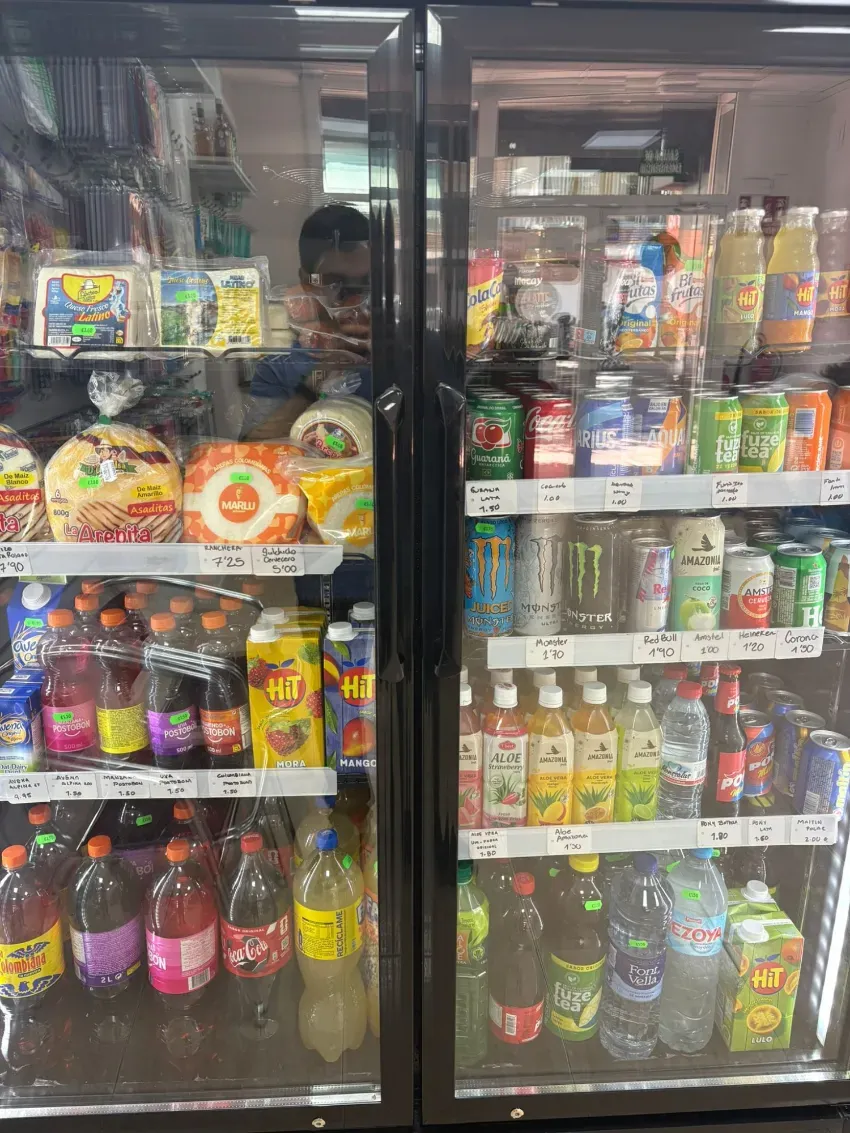 Estantes de un refrigerador con puerta de vidrio, repletos de bebidas, refrigerios y alimentos envasados ​​variados, en una tienda.