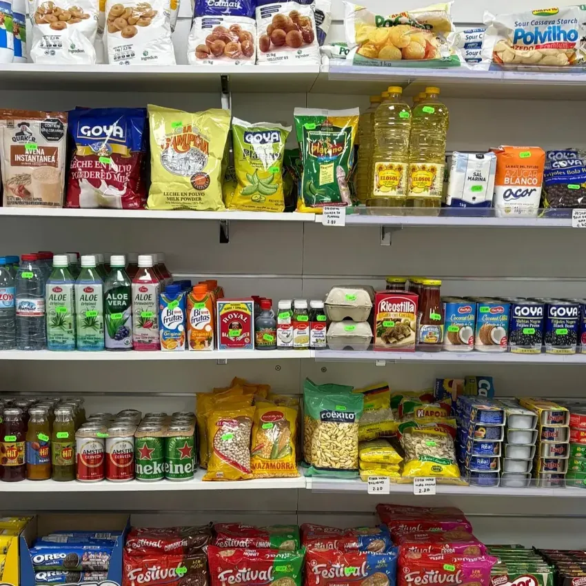 Estantería de la tienda surtida con una variedad de aperitivos envasados, bebidas y productos enlatados, organizados en filas.