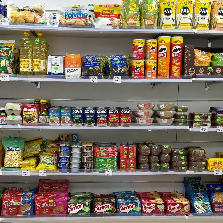 Estantería de supermercado repleta de coloridos aperitivos envasados, latas y tarros dispuestos en filas.