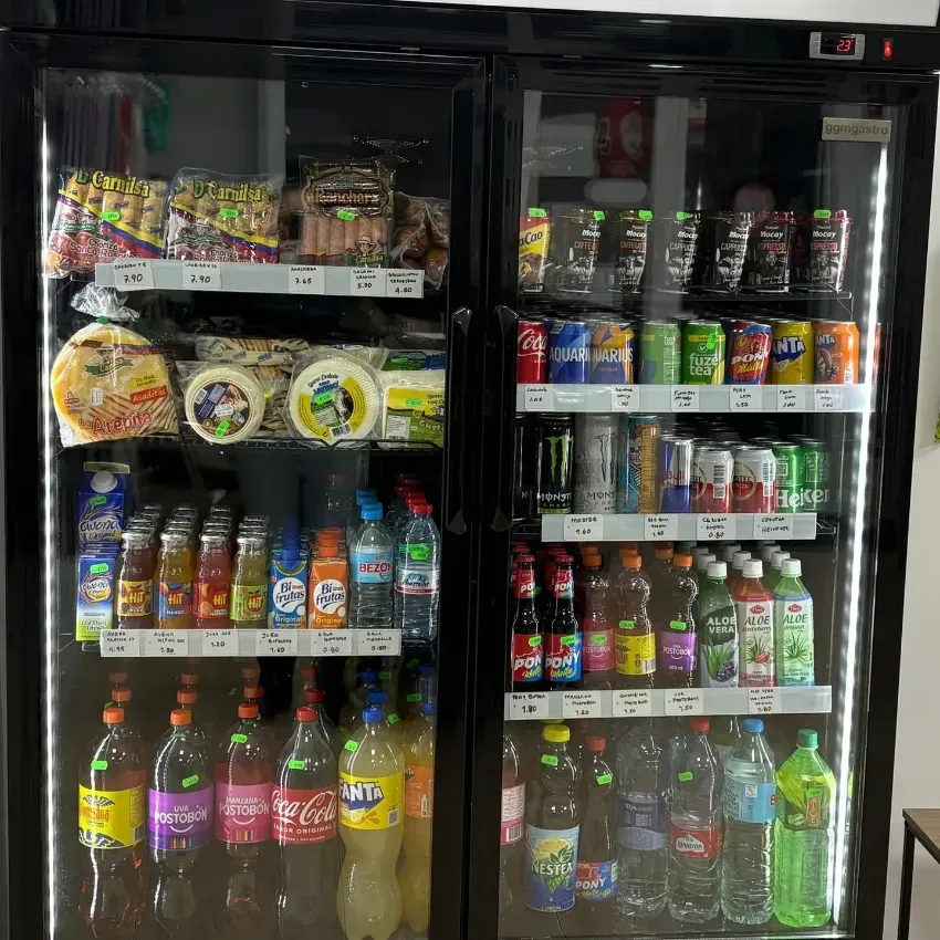 Vitrina refrigerada de tienda de conveniencia con bebidas coloridas y fideos instantáneos en estantes detrás de puertas de vidrio.
