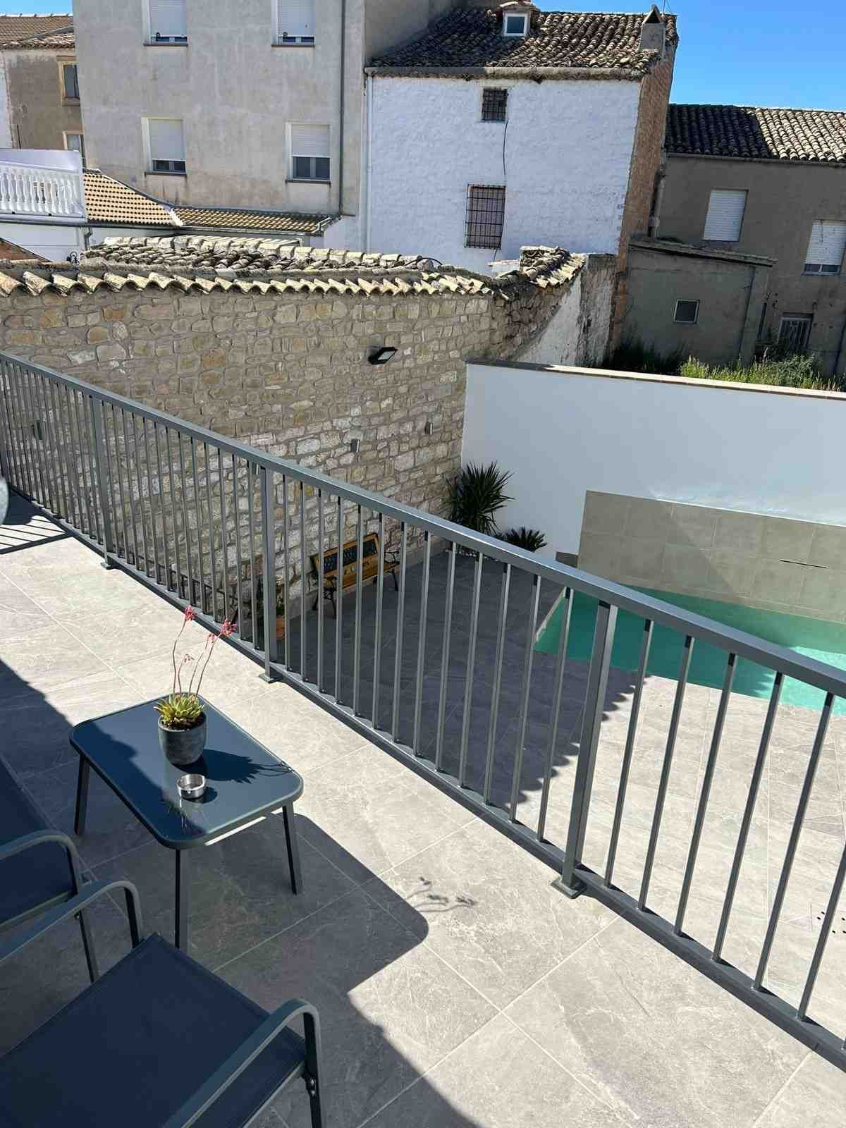 Una terraza con mesa y sillas de metal oscuro con vistas a una pequeña piscina al aire libre y a antiguos edificios de piedra.