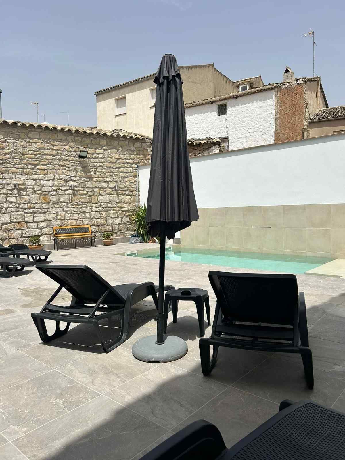 Patio con piscina, dos tumbonas negras y una sombrilla oscura cerrada en un día soleado.