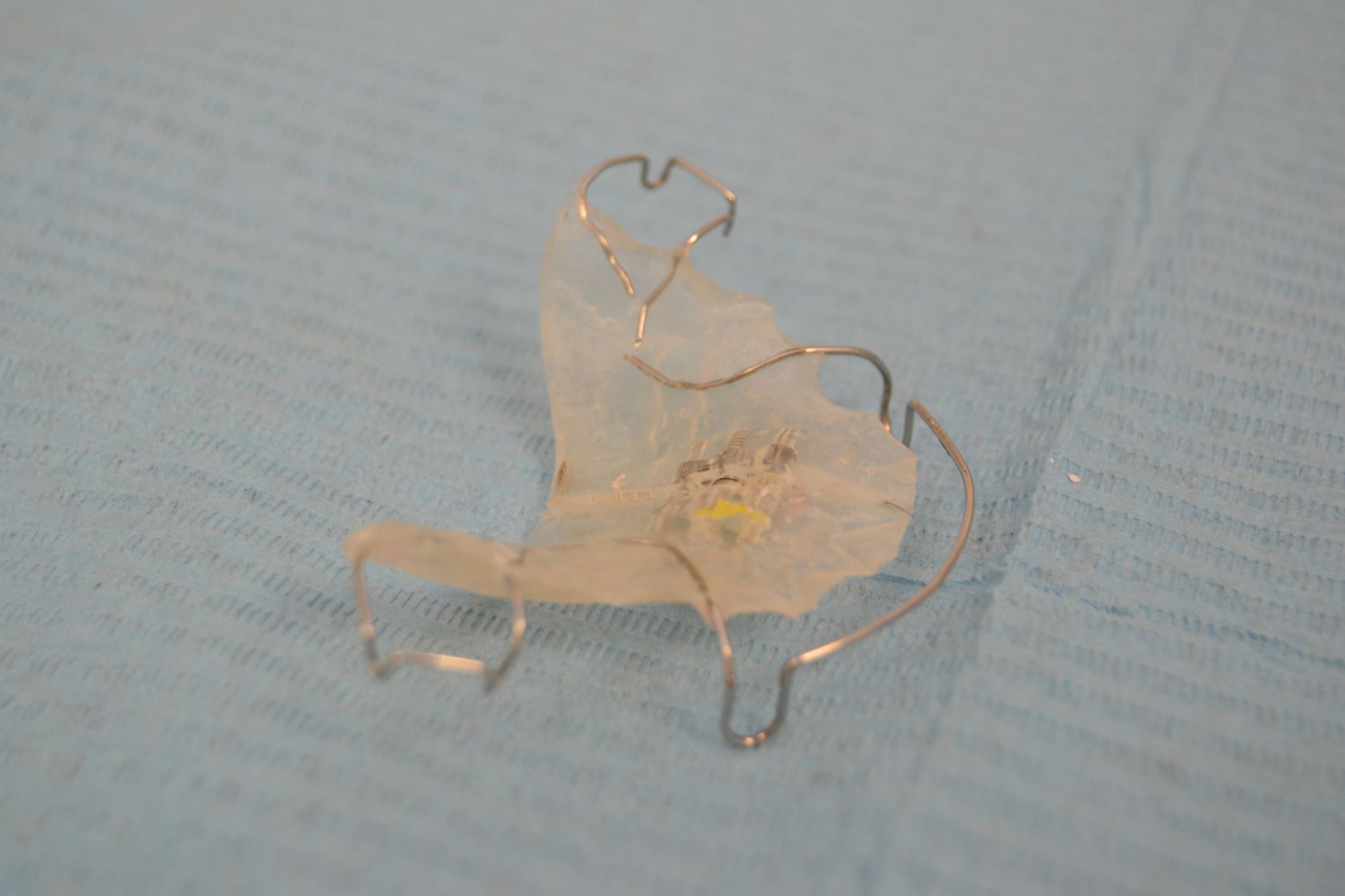 Retenedor de ortodoncia de plástico transparente y alambre sobre una superficie de color azul claro.