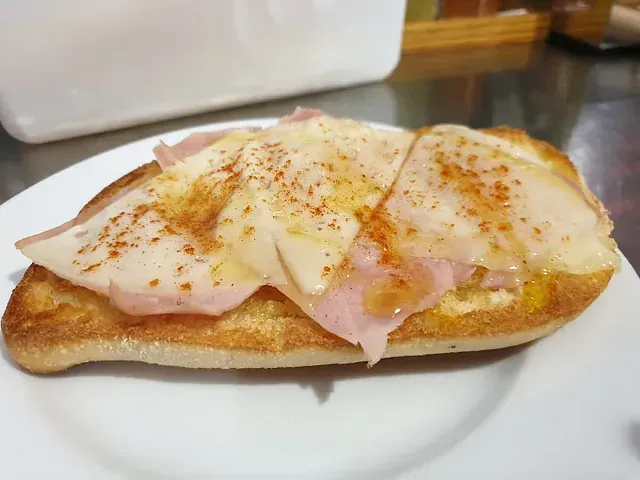 Un sándwich con jamón y queso en un plato blanco.