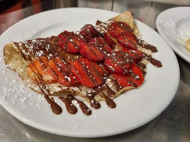 Un plato blanco cubierto con un crepe con fresas y salsa de chocolate.
