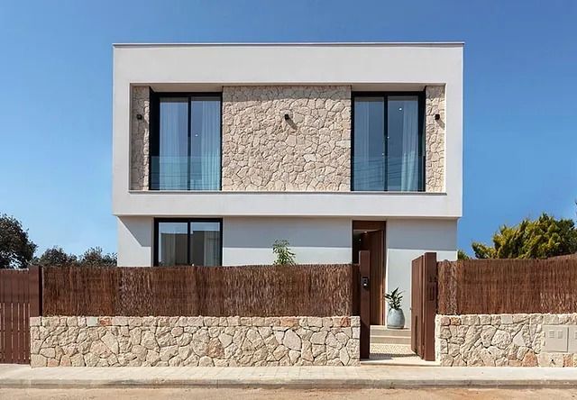 Una casa moderna con un muro de piedra y una valla delante de ella.