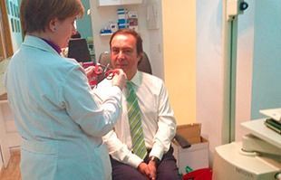 Una mujer con bata de laboratorio está examinando a un hombre con traje y corbata.