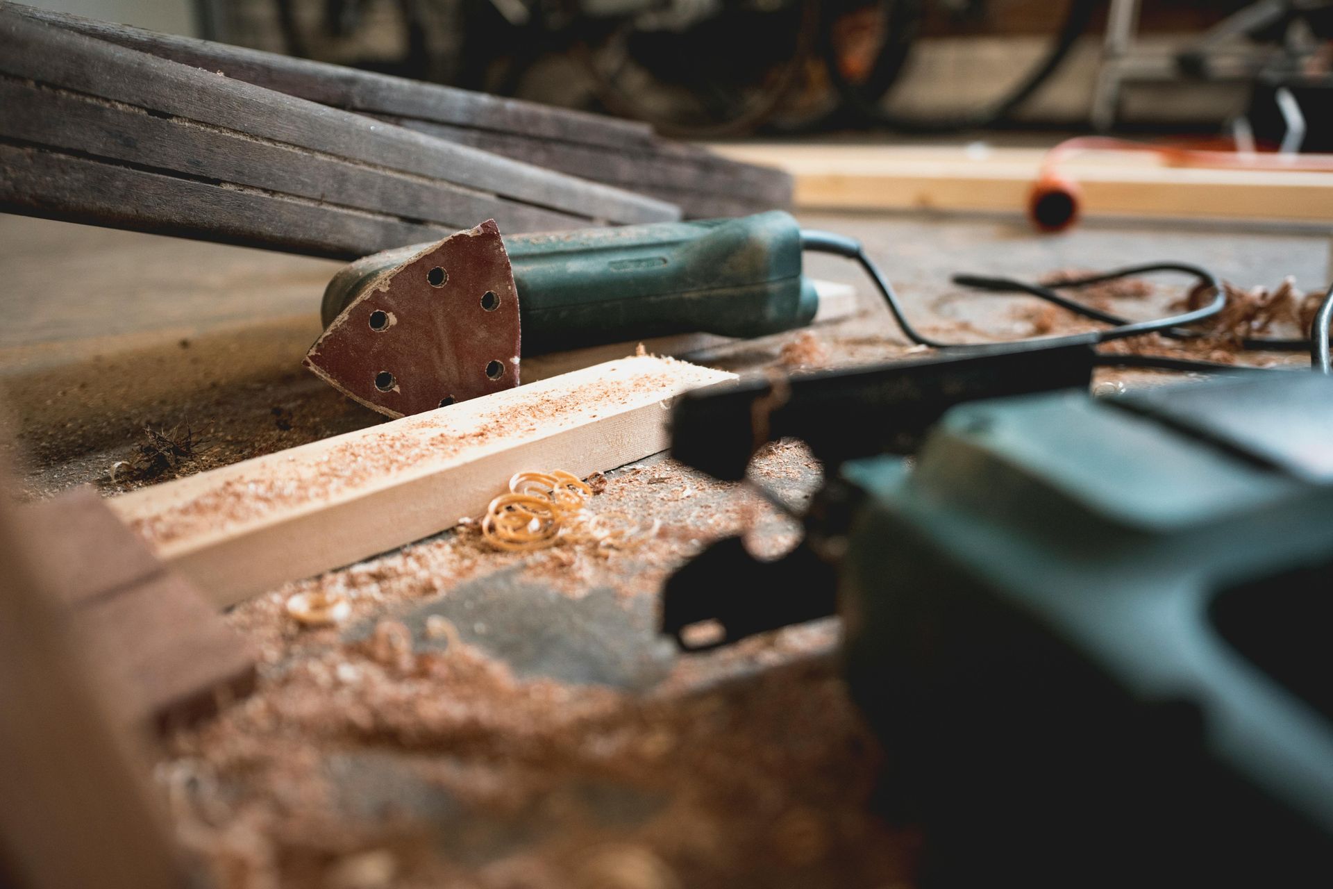Herramientas para trabajar la madera sobre una superficie de trabajo: lijadora, sierra y restos de madera en un garaje.