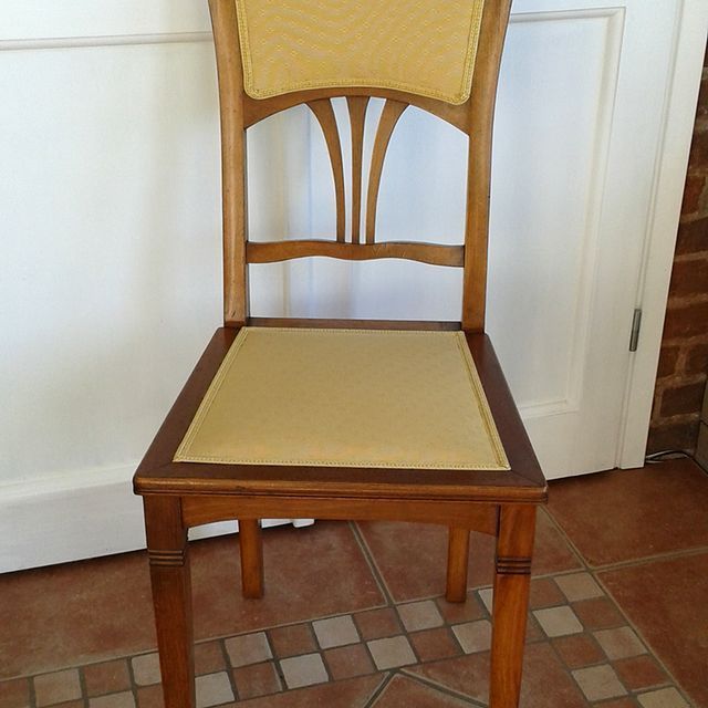 Ein Holzstuhl mit einem gelben Kissen steht auf einem gefliesten Boden