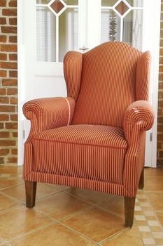 Ein orangefarbener Stuhl steht auf einem gefliesten Boden vor einer Backsteinwand.