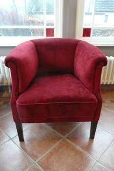 Ein roter Stuhl steht auf einem gefliesten Boden vor einem Fenster.