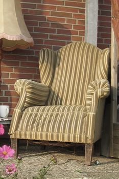 Ein gestreifter Stuhl steht vor einer Backsteinwand neben einer Lampe.