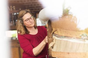 Eine Frau in einem roten Hemd arbeitet an einem Möbelstück.